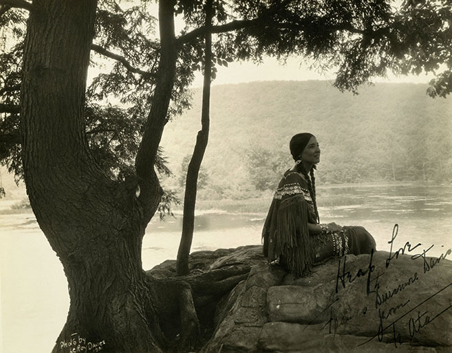 Te Ata in traditional Native American dress, sitting at shore